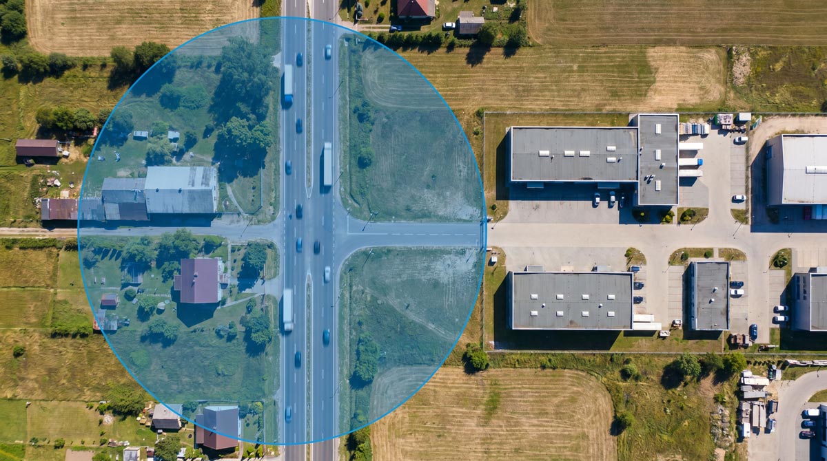 Aerial view of an industrial area with warehouses, parking lots, and a crossroad highlighted by a large translucent blue circle geofence overlay.